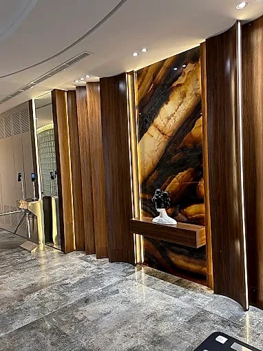 A corridor lined in fluted walnut leading past a backlit onyx niche.