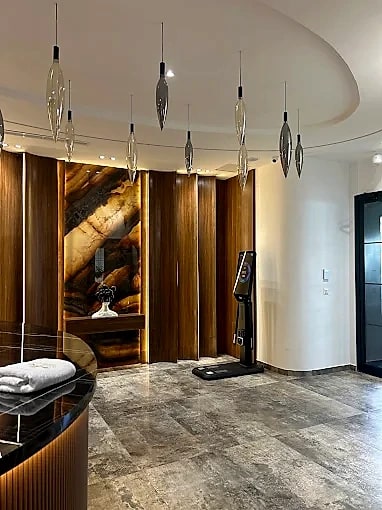 The entrance lobby at Naouar Prestige Gym, with a cluster of hand-blown pendant lights above a backlit onyx wall and marble floor.