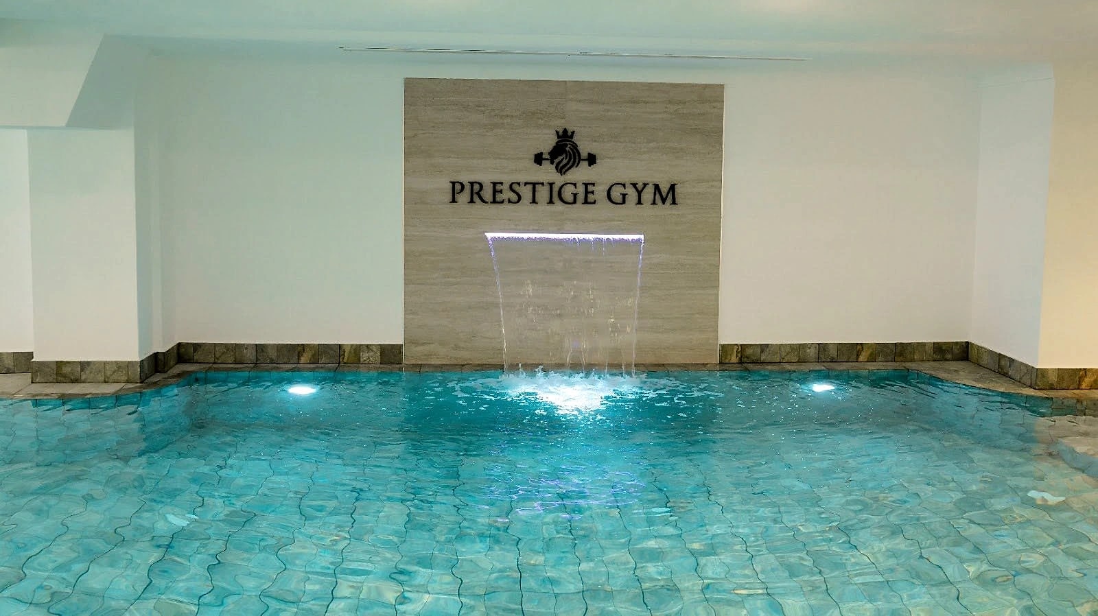 The indoor swimming pool at Naouar Prestige Gym, lit from beneath, with a sheet water feature falling into it.