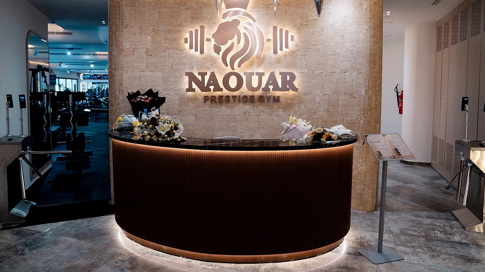 The curved walnut reception desk, the illuminated Naouar mark on the wall behind it.