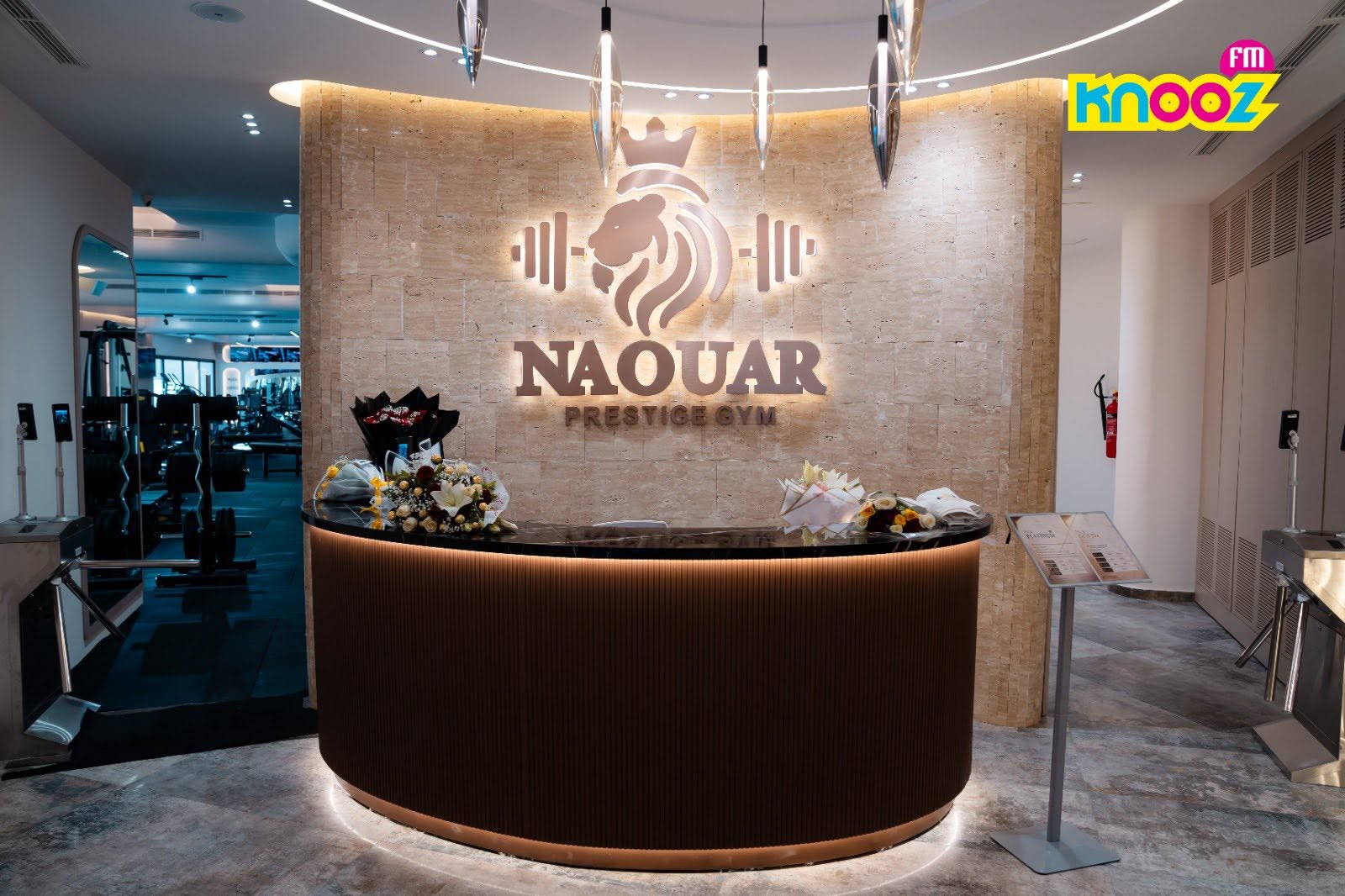 The curved walnut reception desk beneath the illuminated Naouar mark.