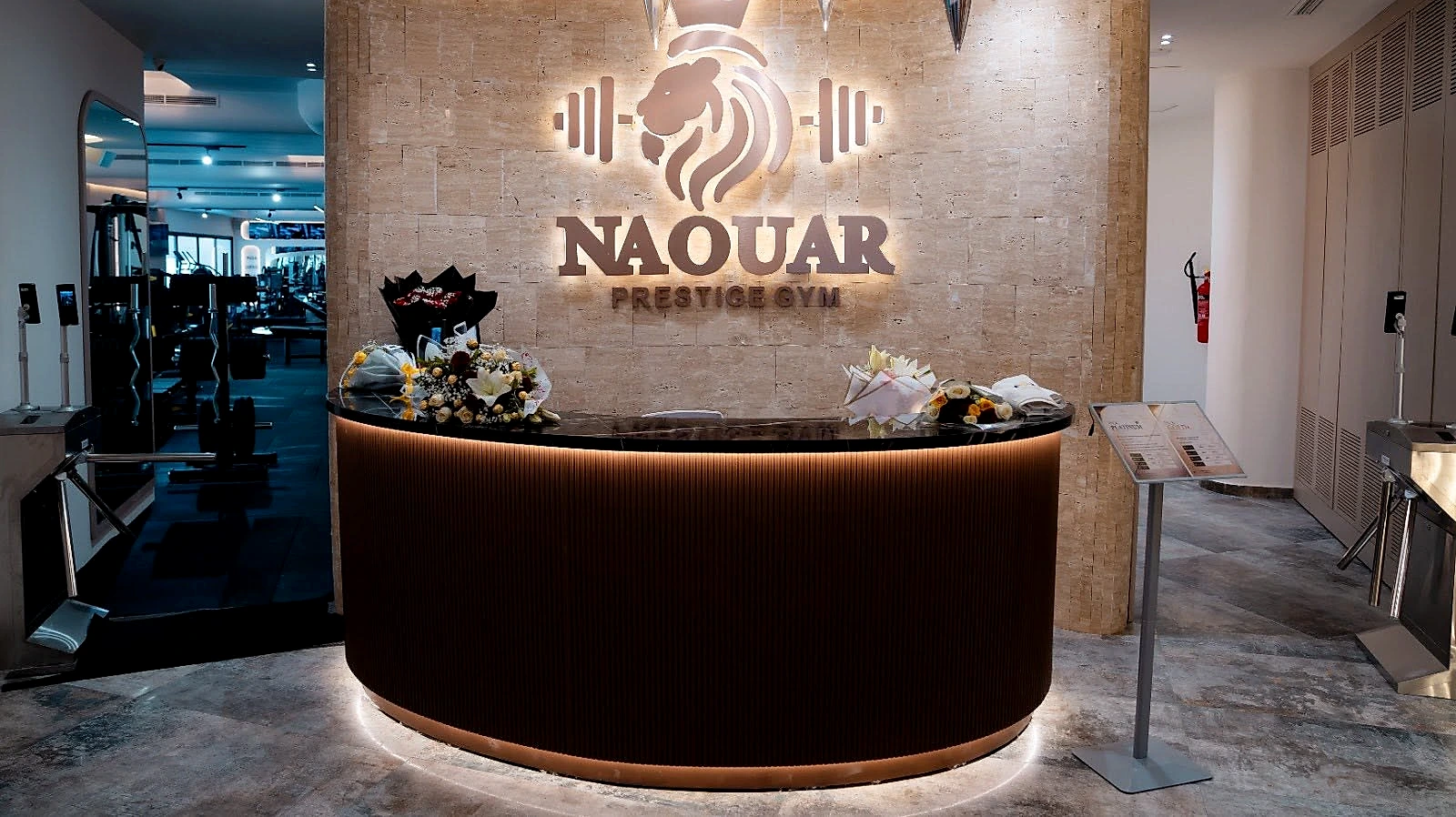 The curved walnut reception desk, the illuminated Naouar mark on the wall behind it.